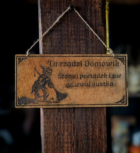Dekoracyjna grawerowana tabliczka ze słowiańskim napisem  „Tu rządzi Domowik. Szanuj porządek i nie gniewaj duszka” –  ozdoba do domu inspirowana folklorem i słowiańskim humorem.