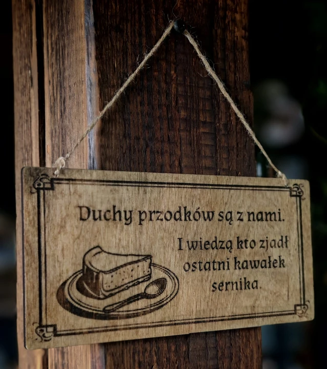 Dekoracyjna grawerowana tabliczka ze słowiańskim napisem „Duchy przodków są z nami. I wiedzą kto zjadł ostatni kawałek sernika” –  ozdoba do domu inspirowana folklorem i słowiańskim humorem.