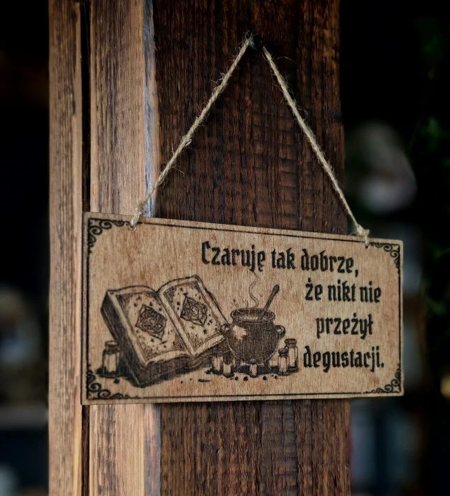 Tabliczka „Czaruje tak dobrze, że nikt nie przeżył degustacji”  Dekoracyjna grawerowana tabliczka ze słowiańskim napisem  –  ozdoba do domu inspirowana folklorem i słowiańskim humorem.
