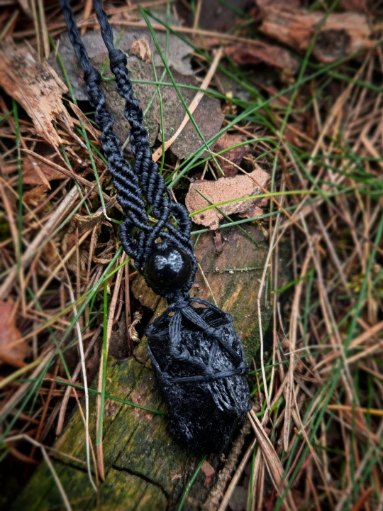 Ręcznie wykonany wisiorek z naturalnym czarnym turmalinem, opleciony czarnym sznurkiem w stylu makramy. Surowy, ciemny kamień pięknie łączy się z głęboką czernią plecionki oraz czarnym koralikiem, tworząc mroczny, wyrazisty dodatek.